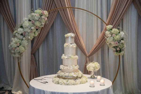 four-tiered wedding cake in front of a gold and floral moon gate