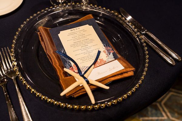 wedding reception place setting with glass charger plate, rust colored napkin and a starfish