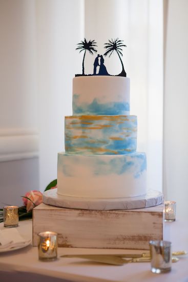 three-tiered wedding cake decorated in brushed gold and tropical blues with a custom cake topper