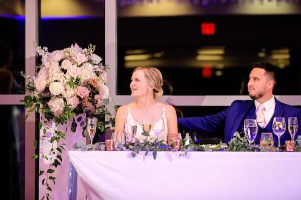 Bride and groom looking on as their wedding party shares toasts