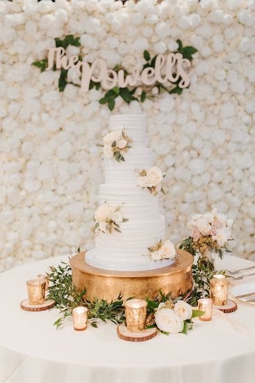 white wedding cake with gold riser and floral wall decor