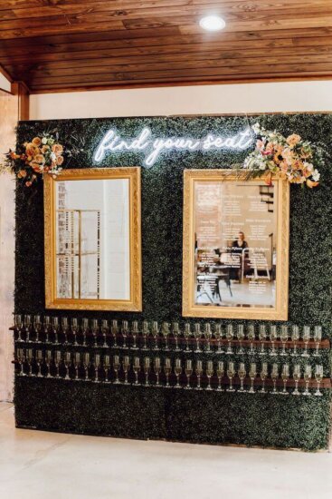 Boxwood wall with seating chart and glasses of champagne