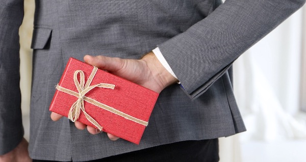 man in a suit holding a box with an engagement ring behind his back