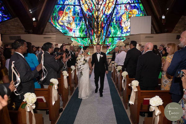 Bride and groom exiting church while guests wave ribbon wands