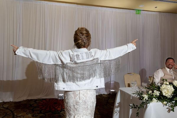 Bride making her entrance wearing a bedazzled BRIDE jacket with rhinestone fringe