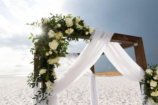 Wooden ceremony structure draped in white fabric with white flowers