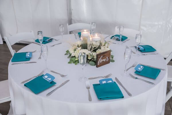 Beach wedding reception set with white linens, teal colored napkins and floating candles