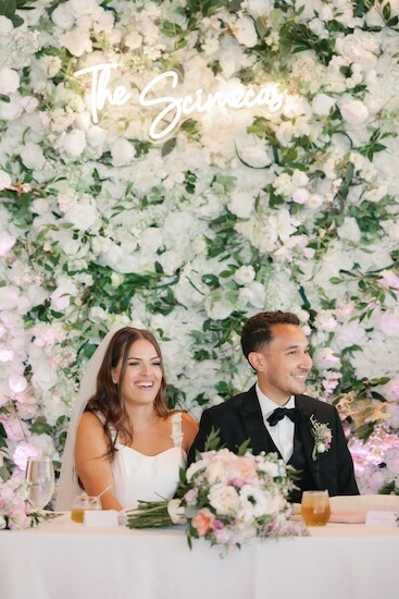 Bride and groom at their sweetheart table in front of a floral wall