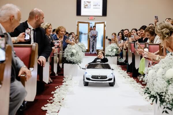 Ringbearer making his way down the aisle in a toy car