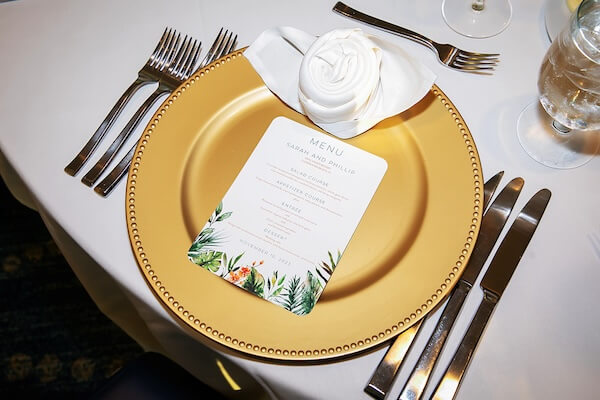 Wedding place setting with a gold charger plate, menu card and rose napkin fold.