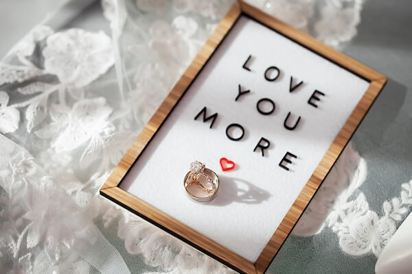 Wedding ring shot on a board reading Love You More