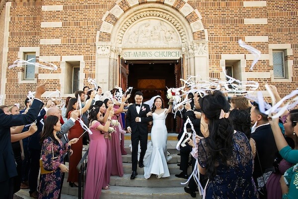 Bride and groom's leaving the wedding ceremony with people waving ribbon wands.