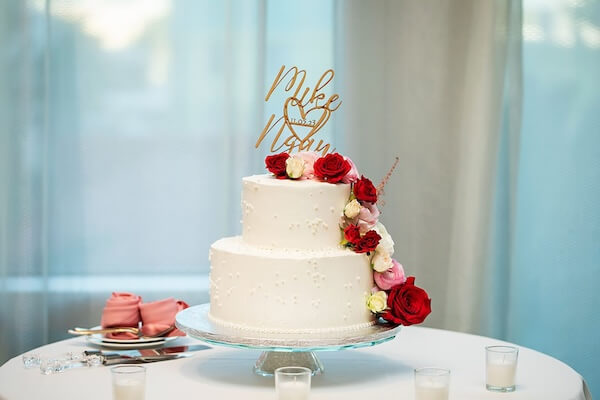 Two-tiered white wedding cake with fresh flowers and a custom cake topper.