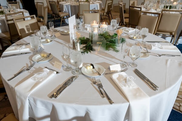 Wedding reception tables set with white linens, floating candles, and holiday greenery.