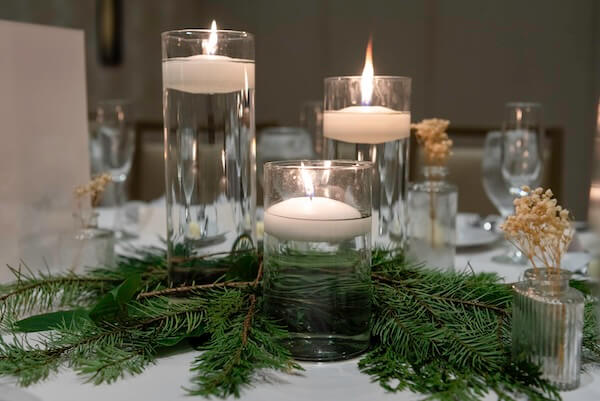 Wedding reception tables set with white linens, floating candles, and holiday greenery.