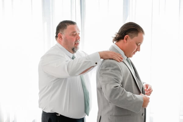 A groom getting a little helps with his jacket.