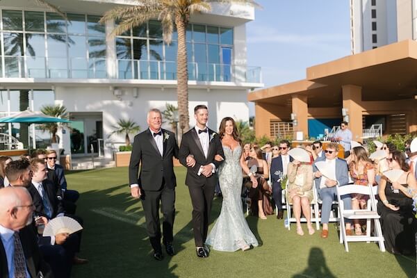 A groom and his parents walking down the aisle on the event lawn at the Opal Sands Resort.
