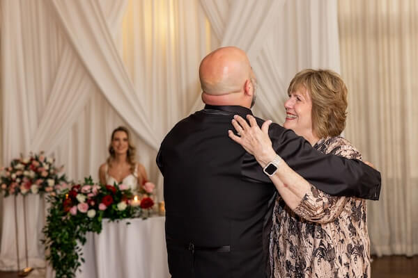 A groom dancing with his mother as his birde looks on.