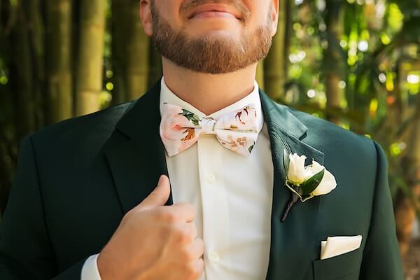 A groom in a green suit with a white floral bow tie.