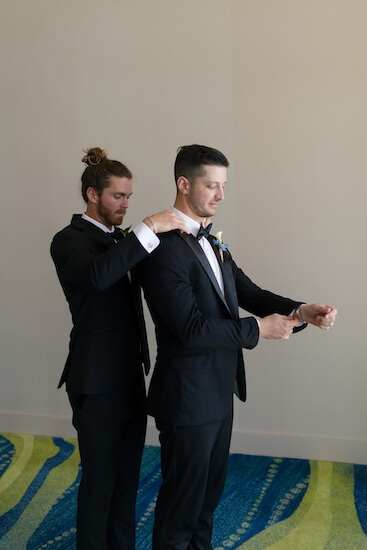 The best man helping the groom get dressed.