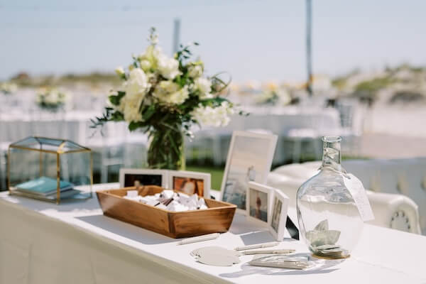 A table with photos of the bride and groom, a guest book and wedding favors for their beach wedding.