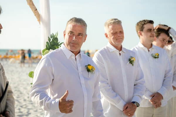 A groom giving a thumbs up as his bride walks down the aisle.