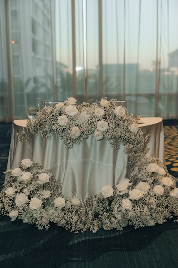 A sweetheart table dressed in white satin linen with white roses and baby's breath.