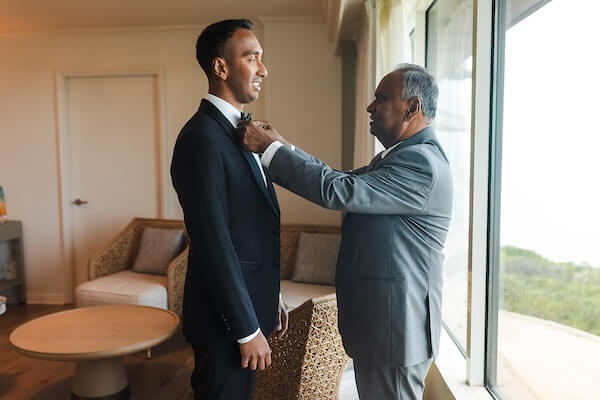 The father of the groom helping him fix his bowtie.