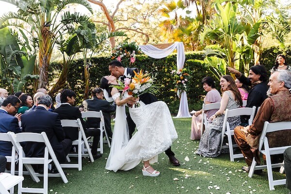 A birde and groom stopping for a kiss on their way up the aisle.
