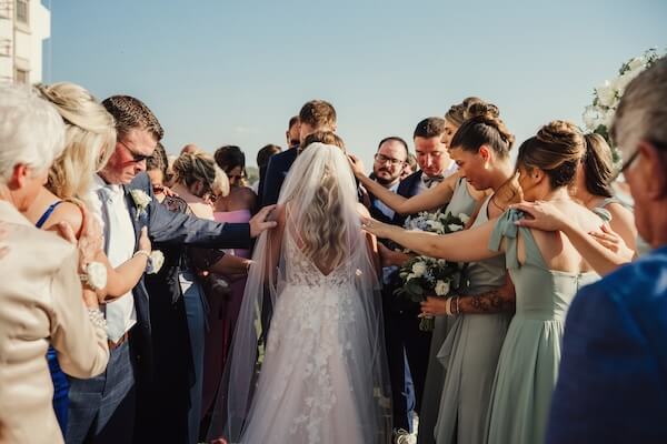 Family and friends surrounding a newlywed couple in prayer during their Opal Sands wedding.